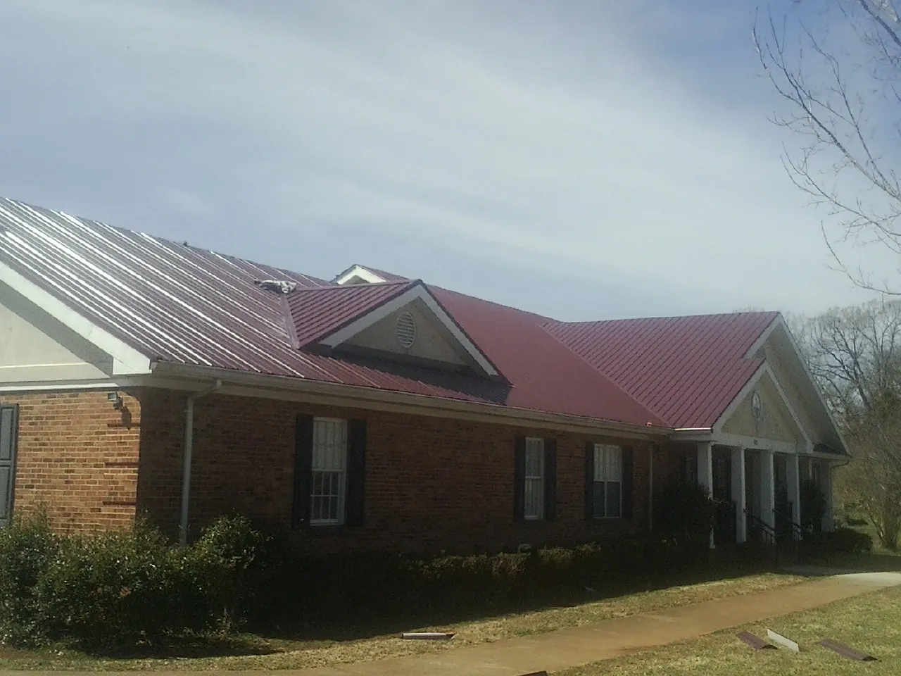Red metal roof with gabled entries on a long brick building, from a Hail Damage Roof Repair job in Parrottsville