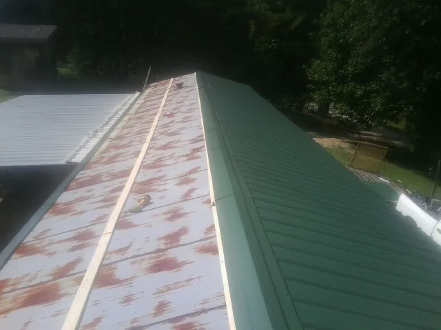 Old rusted panels beside newly installed green metal roofing — Wind Damage Roof Repair by Roofing Brothers in Parrottsville