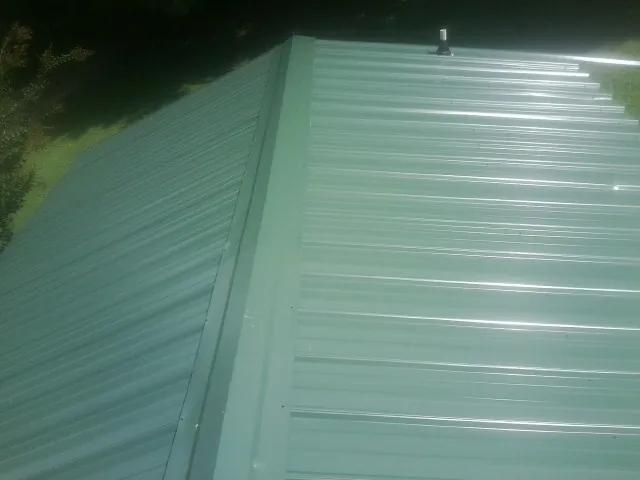 New green metal panels meeting at the ridge of a roof — Flat Roof Repair work by our crew in Parrottsville