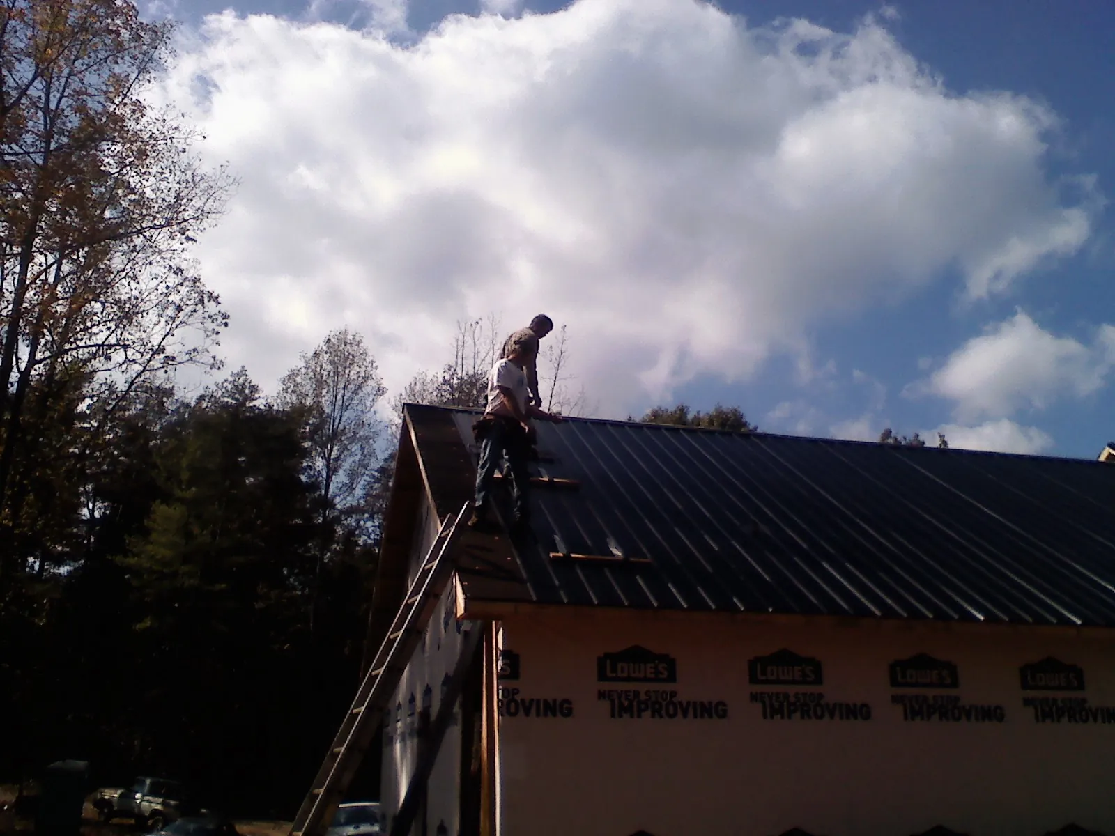Roofer fastening dark metal panels high against a cloudy sky, from a Roof Inspection job in Parrottsville