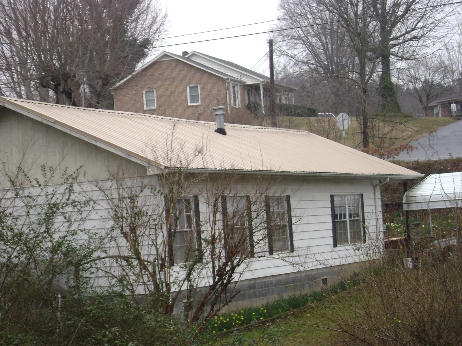 Tan metal roof on a white sided house set into a hillside — Commercial Roofing by Roofing Brothers in Parrottsville