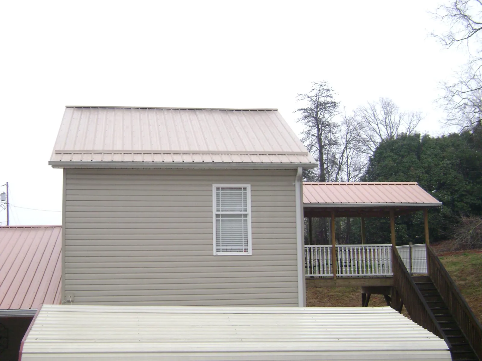 Tan metal roofs on a two story addition and attached porch, from a Roof Replacement job in Parrottsville
